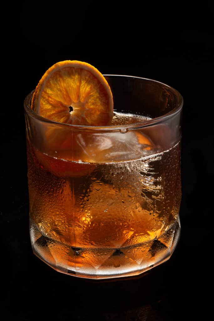 Misted glass of Alcoholic cocktail Old fashioned cocktail with orange slice, bourbon on black background.